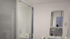 A modern bathroom with a glass shower enclosure, a toilet, a sink with a mirror above, and dark wood flooring. - The Bog Roy Inn (Inverness)