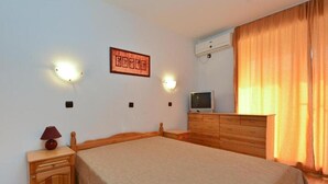 A bedroom with a bed, a dresser, a nightstand, a wall-mounted TV, and a wall-mounted air conditioner. - Laguna Holiday (Sunny Beach)