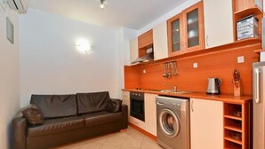 A compact kitchen with a washing machine, a stove, and wooden cabinets. - Laguna Holiday (Sunny Beach)