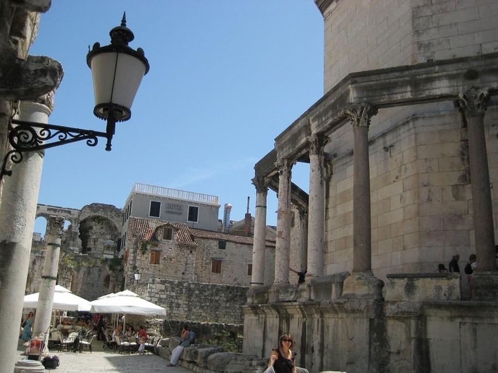 An outdoor area with stone columns, a street lamp, and a building with arches.