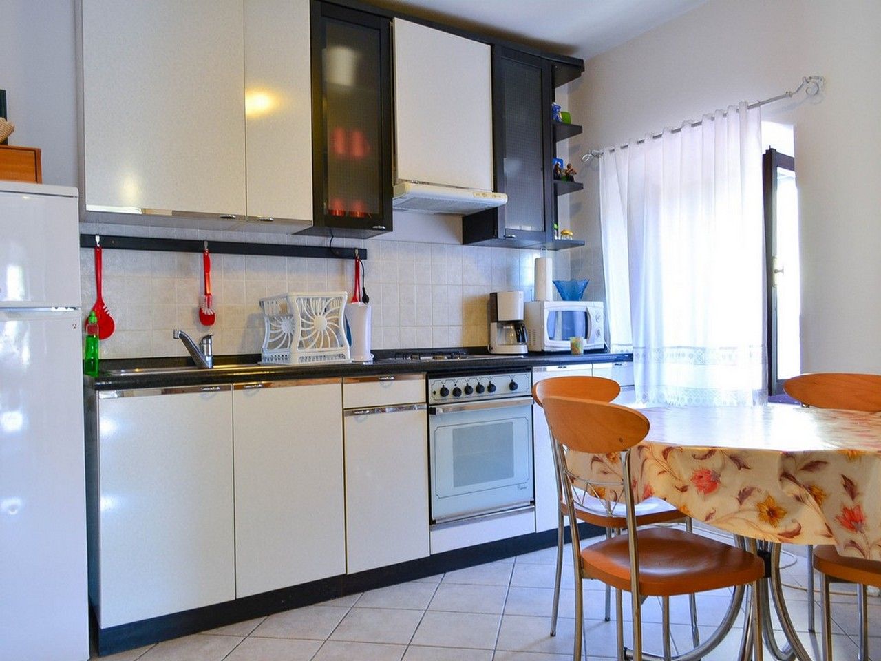 A kitchen with white cabinets, a stove, a microwave, and a dining area with a table and chairs.