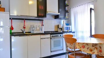 A kitchen with white cabinets, a stove, a microwave, and a dining area with a table and chairs.