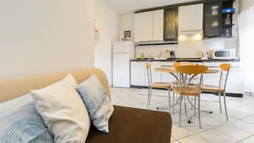 A compact living space with a sofa, a dining table with chairs, a kitchen area with appliances, and a small refrigerator.