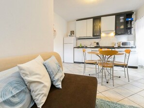 A compact living space with a sofa, a dining table with chairs, a kitchen area with appliances, and a small refrigerator.