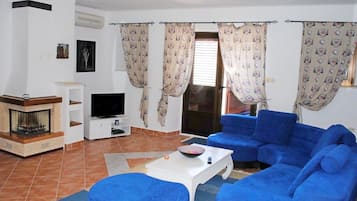 A living room with a fireplace, a TV, blue sofas, and patterned curtains.