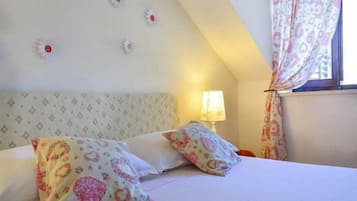 A bedroom with a bed, pillows, a nightstand, a lamp, and a window with curtains.