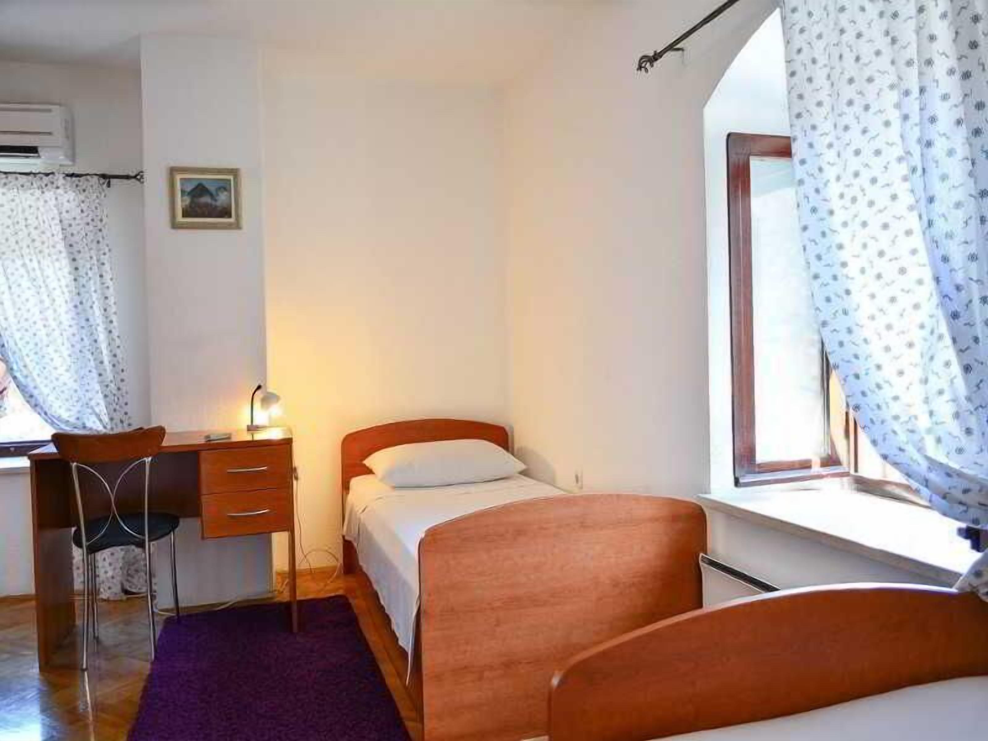 Un dormitorio con una cama, un escritorio con silla, una ventana con cortinas y un cuadro pequeño en la pared.