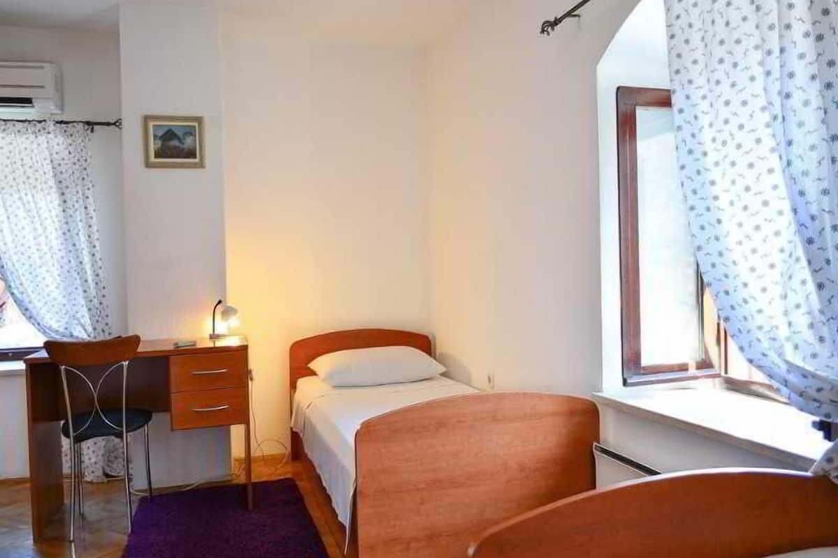 A bedroom with a bed, a desk with a chair, a window with curtains, and a small picture on the wall.