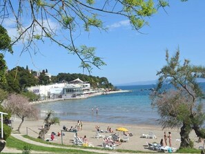 A beach with people sunbathing, a building with a white facade, and a clear blue sky.
