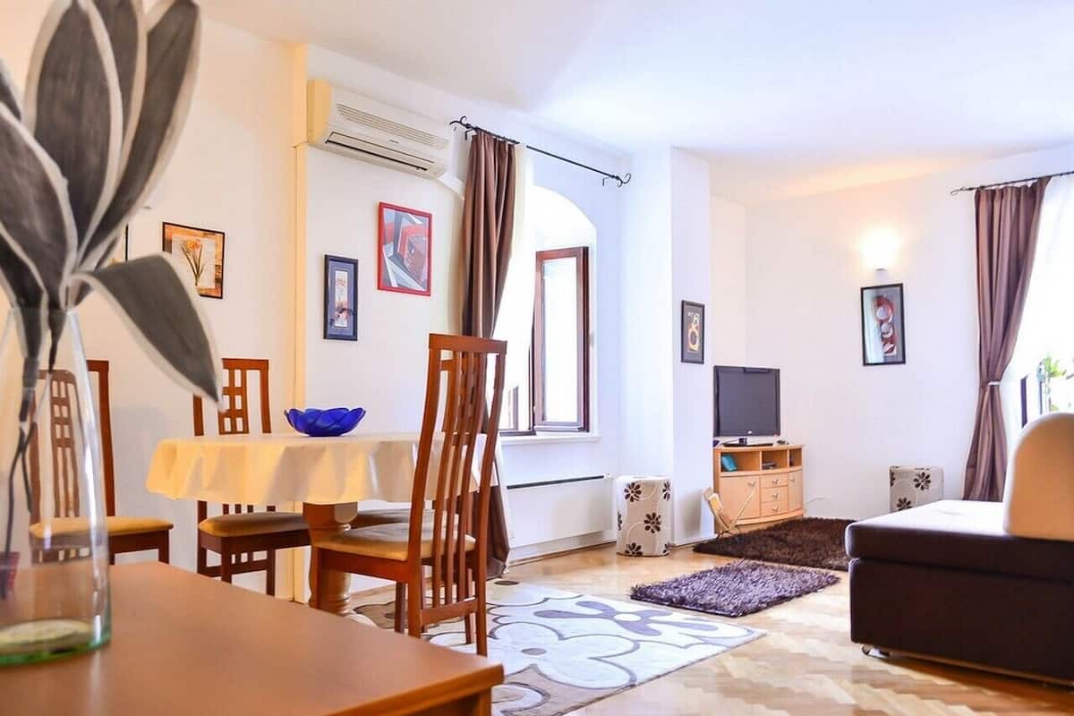 A living room with a dining area, a sofa, a TV, and a window with curtains.
