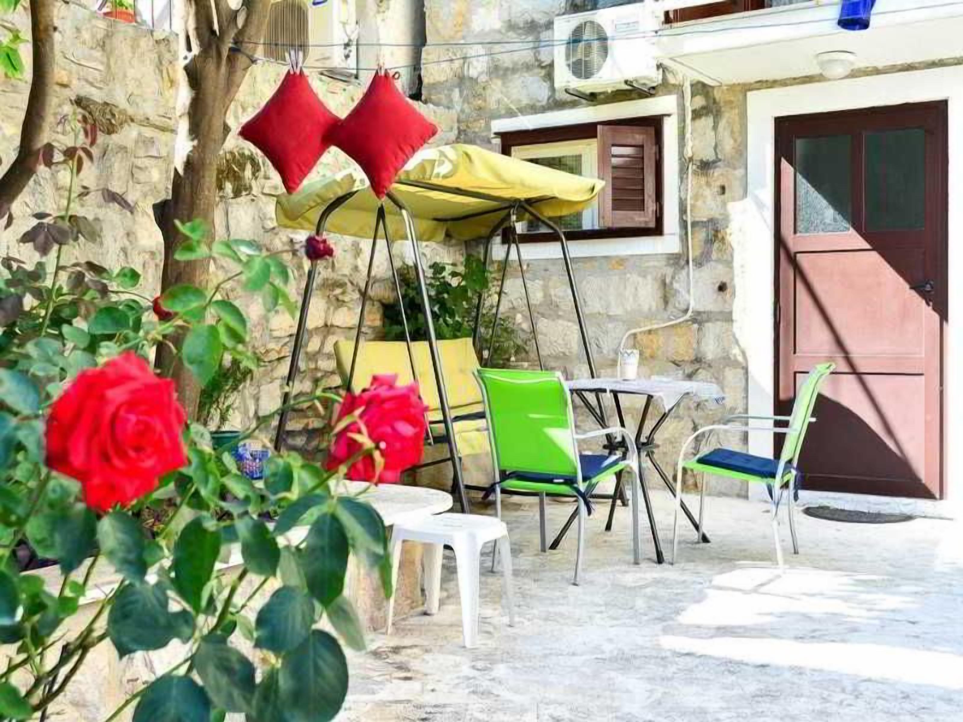 An outdoor seating area with a table and chairs, a yellow umbrella, and a red door in the background.