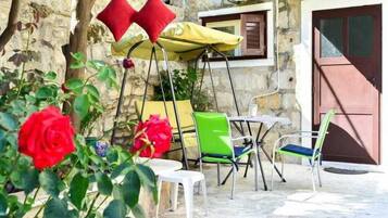 An outdoor seating area with a table and chairs, a yellow umbrella, and a red door in the background.