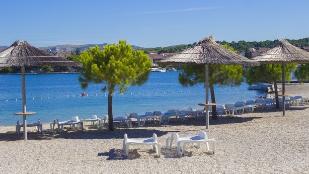 A beach with thatched umbrellas, white plastic chairs, and a clear view of the sea. - Hotel Spongiola (Sibenik)