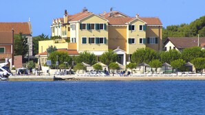A multi-story hotel with a yellow facade, green shutters, and a beachside location. - Hotel Spongiola (Sibenik)