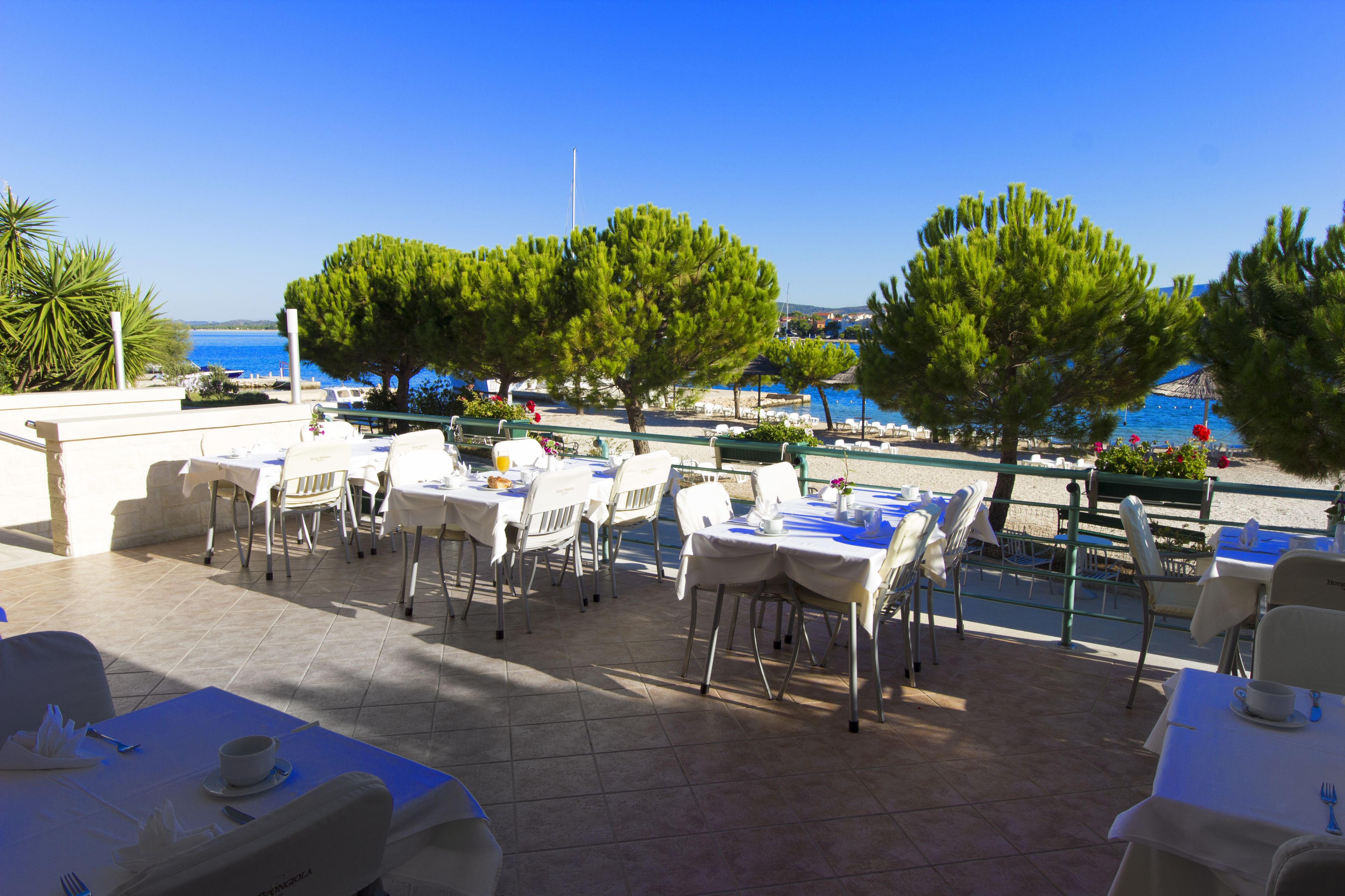 An outdoor dining area with tables and chairs, overlooking a body of water.