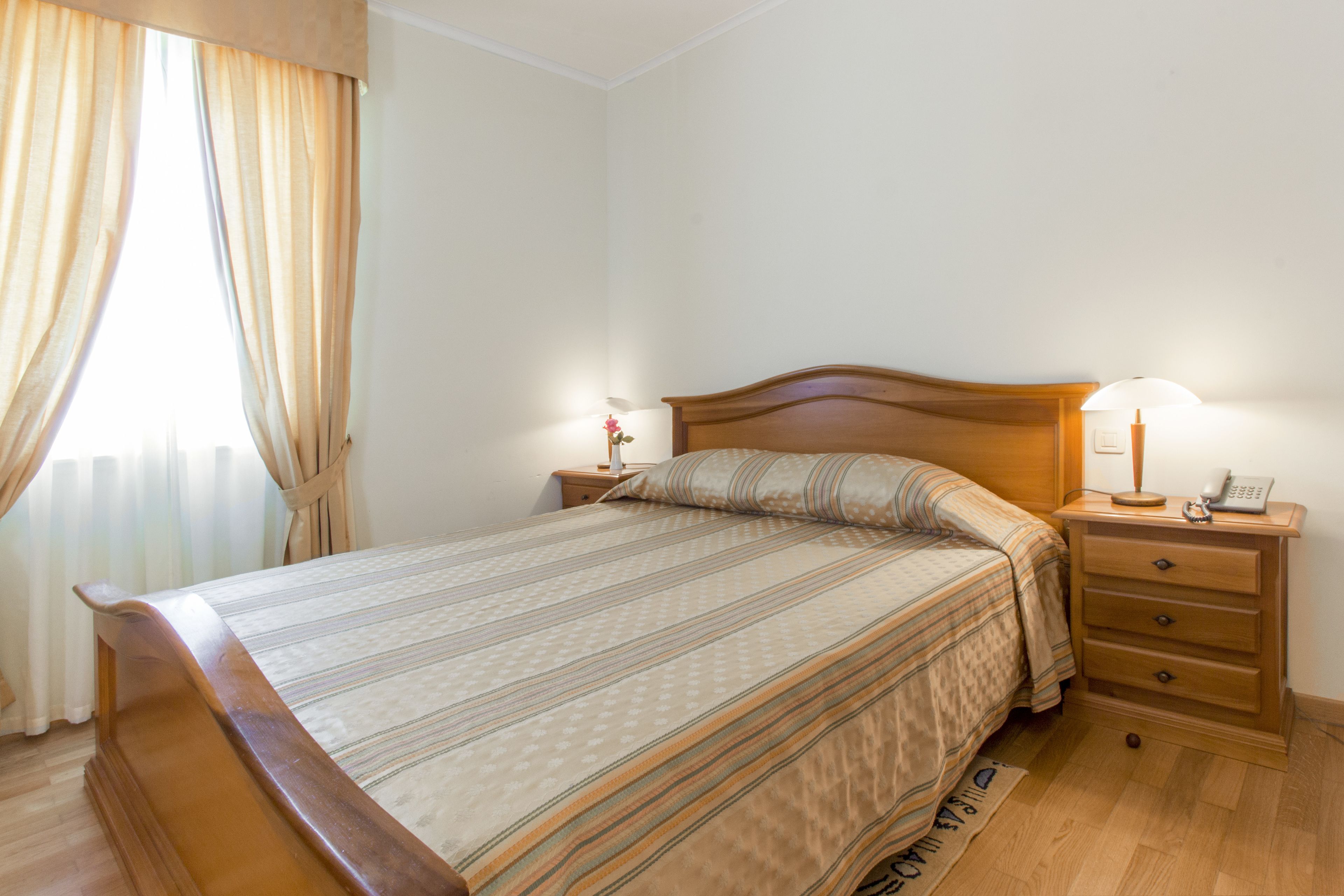 A neatly made bed with a wooden headboard, two bedside tables with lamps, and a window with curtains.