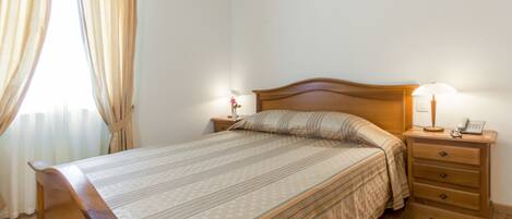 A neatly made bed with a wooden headboard, two bedside tables with lamps, and a window with curtains.