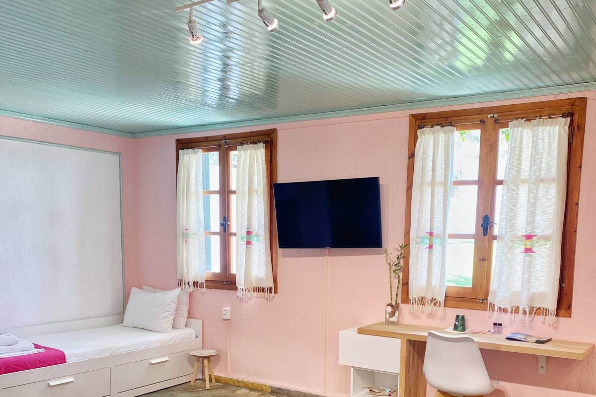 A room with a bed, a desk, a chair, a TV, and a window with curtains.