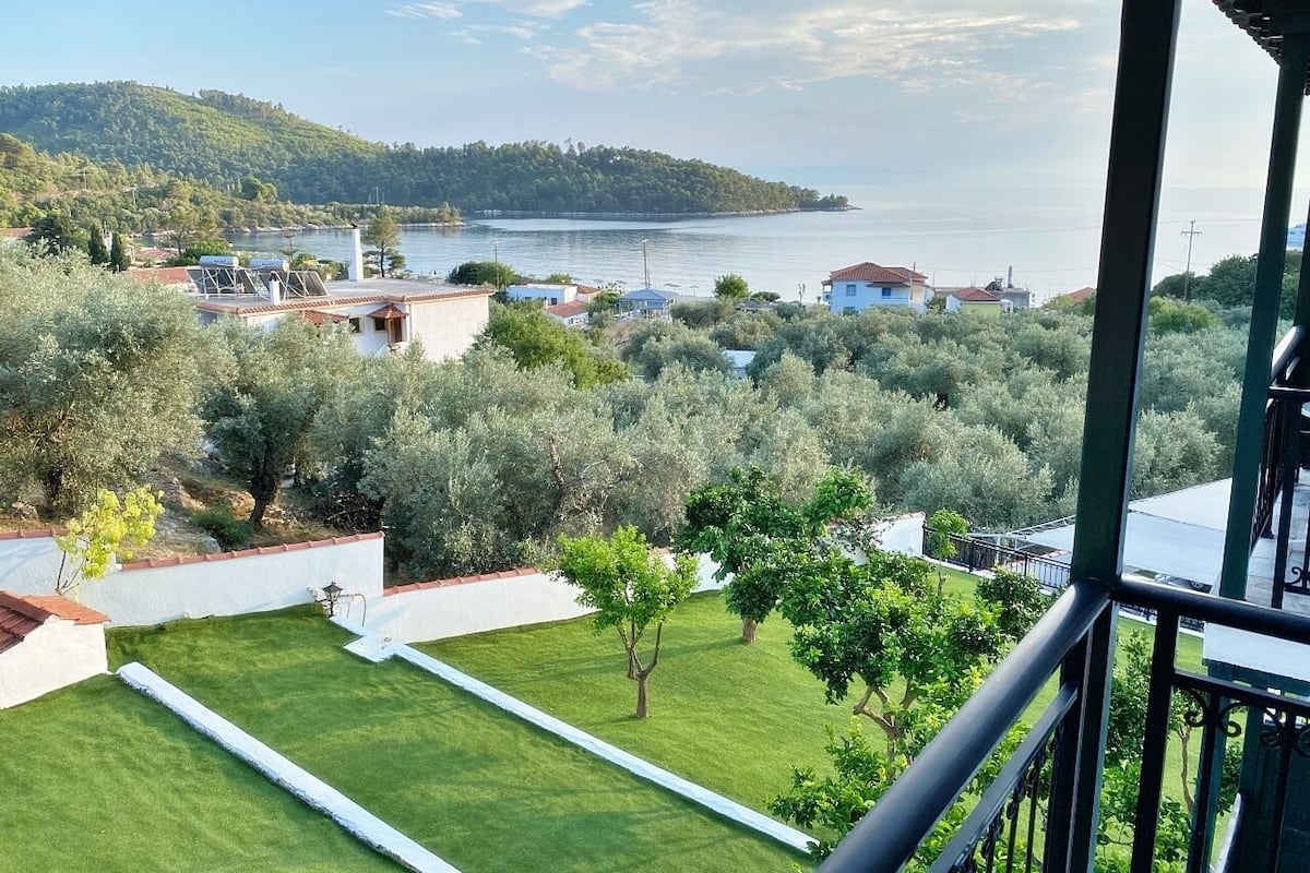 A balcony with a view of a coastal town, a grassy area, and a hill in the distance.