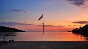 Een strand met een vlag, rustig water en een zonsondergang.