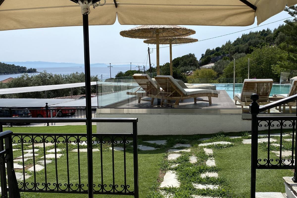 A poolside area with lounge chairs and umbrellas, a stone pathway, and a view of the sea.