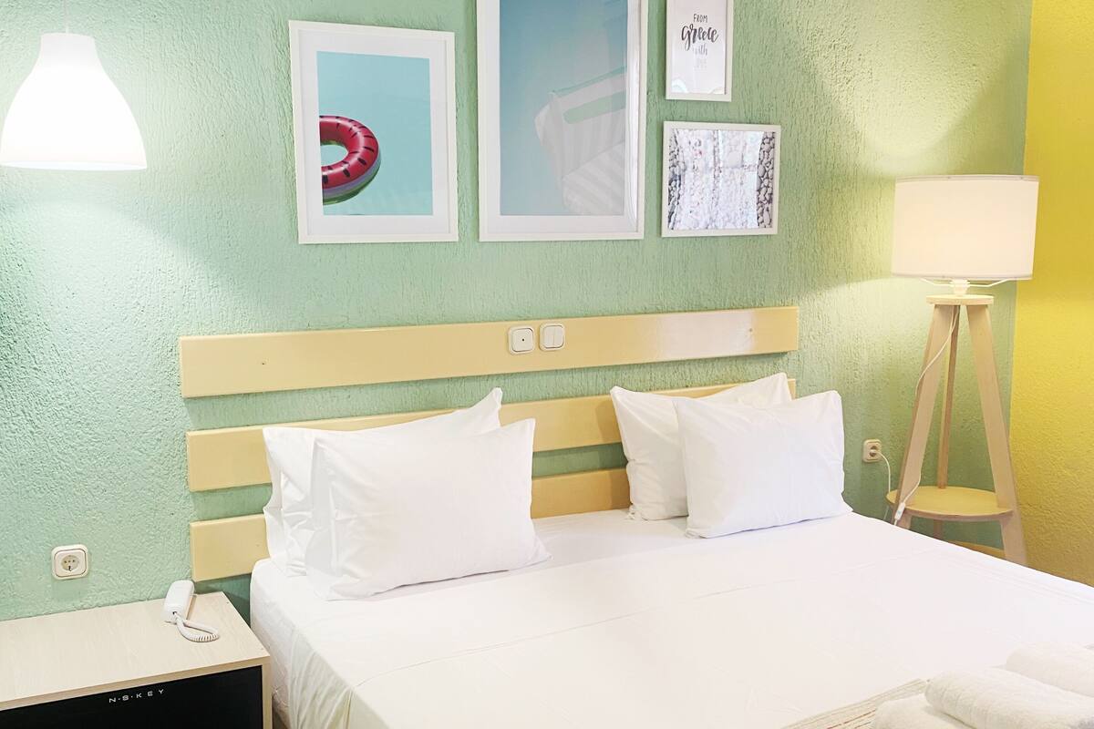 A hotel room with a bed, a nightstand, a lamp, and wall art.