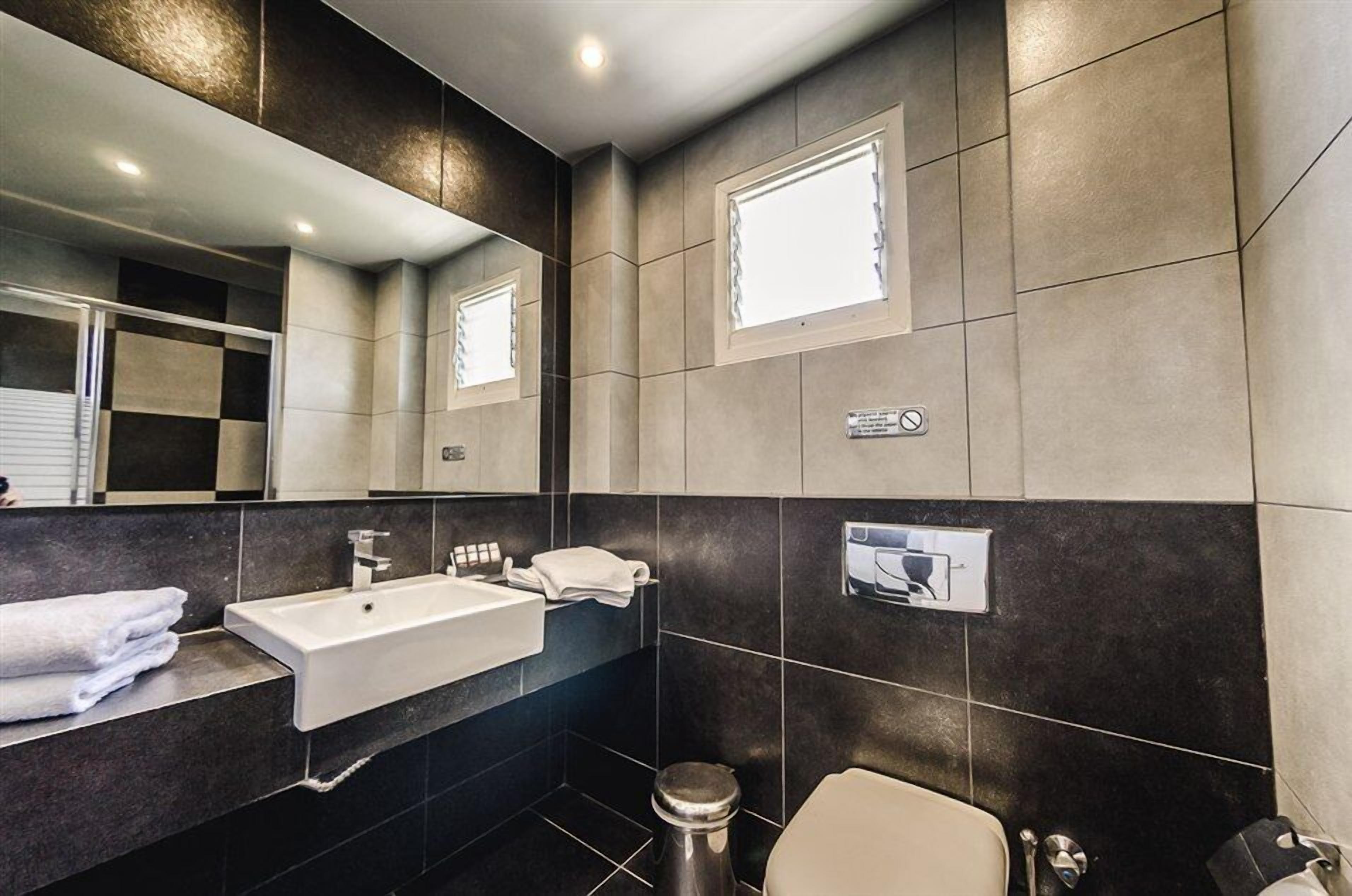 Een moderne badkamer met een grote spiegel, een wit wastafelmeubel, een toilet en een prullenbak.