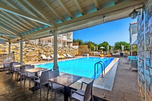 Un área junto a la piscina con sillas de descanso, piscina y una zona de estar cubierta con mesas y sillas.