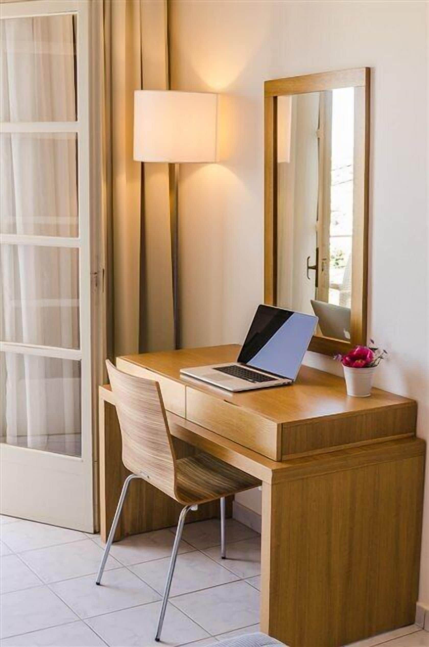 A wooden desk with a laptop, a chair, a lamp, and a mirror.