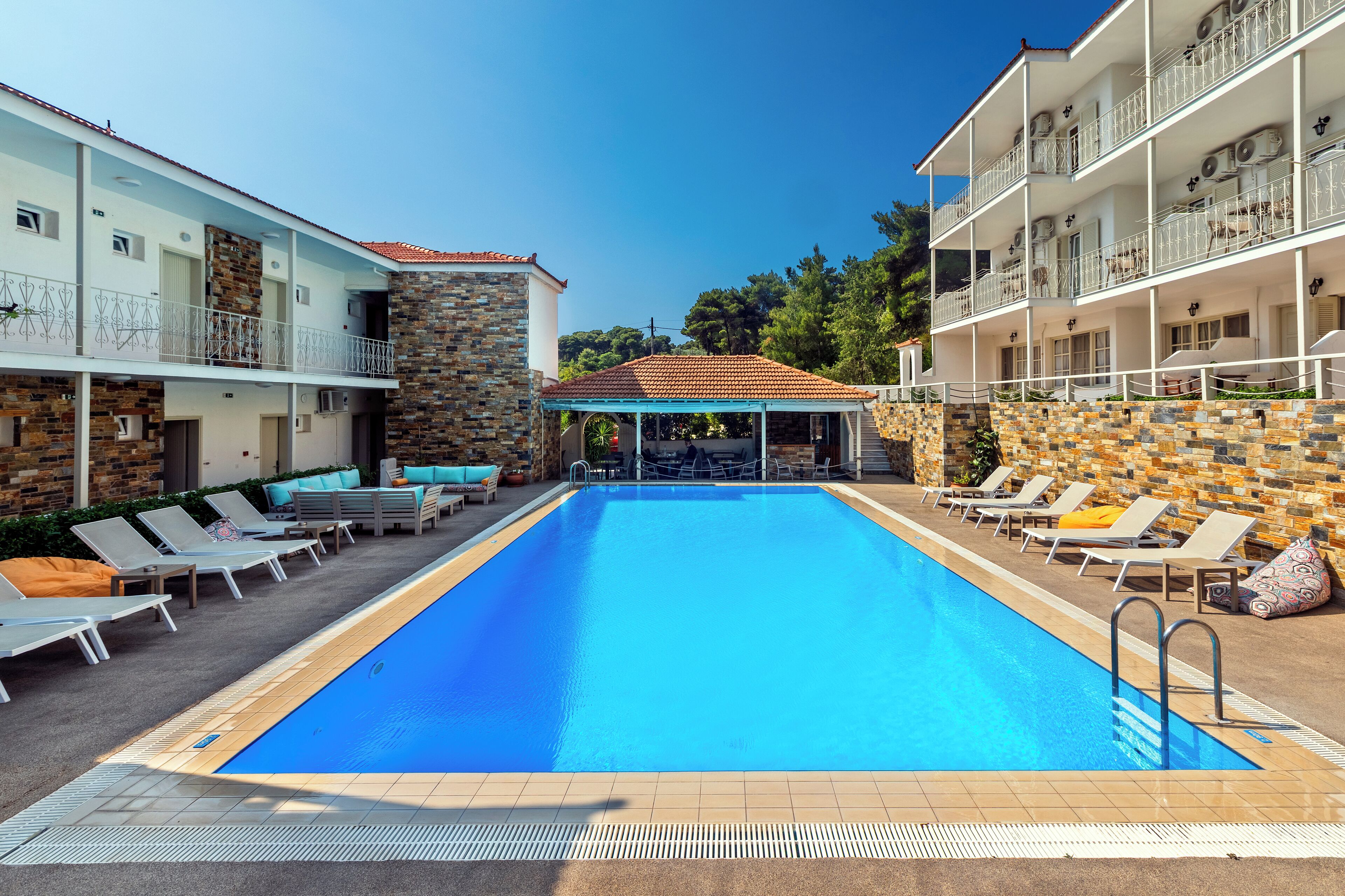 A swimming pool with lounge chairs and a covered area, surrounded by multi-story buildings with balconies.