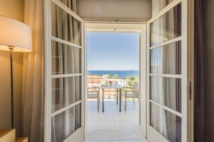 Un balcón con mesa y sillas, vista al mar y una lámpara a la izquierda.