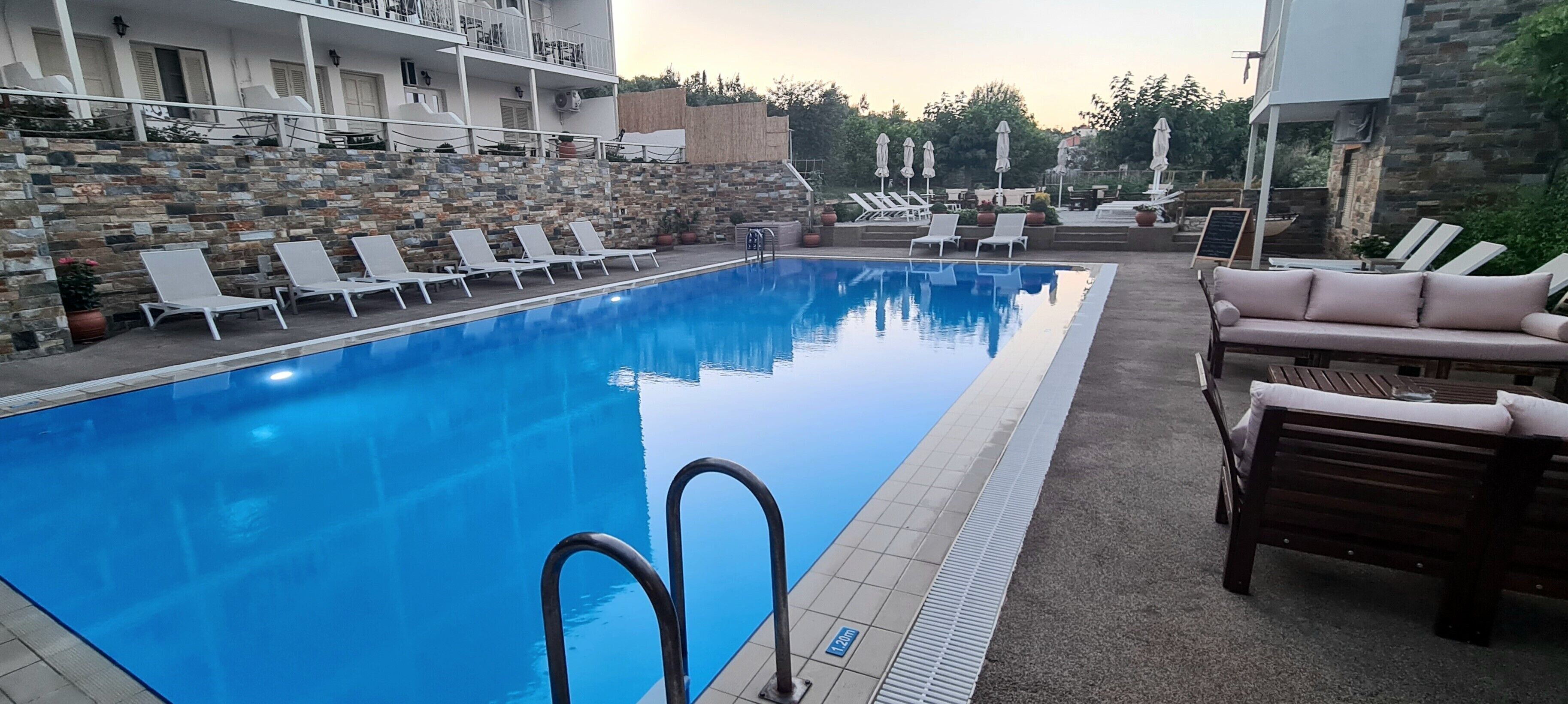 A swimming pool with lounge chairs and a sofa, surrounded by stone walls and a balcony.