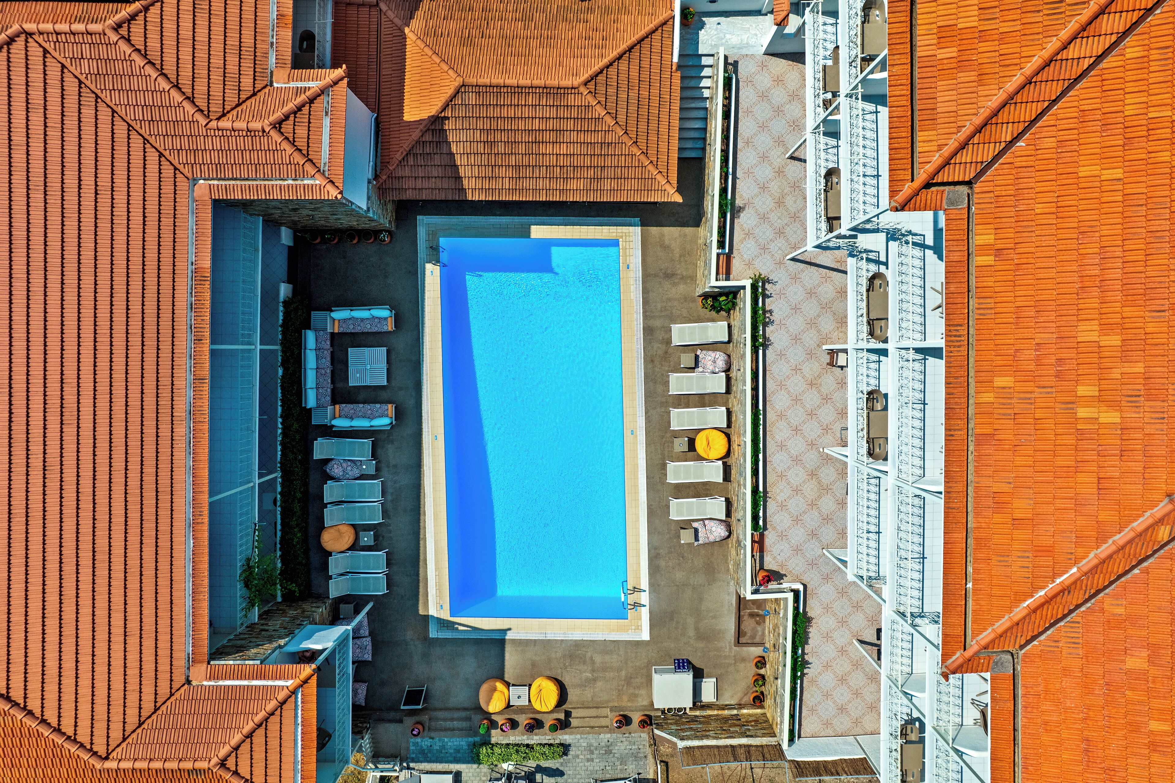 An aerial view of a hotel with a swimming pool surrounded by sun loungers and a small bar area.