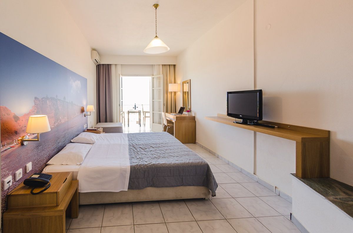 Une chambre d’hôtel avec un grand lit, un bureau avec un ordinateur, une télévision et un tableau au mur.