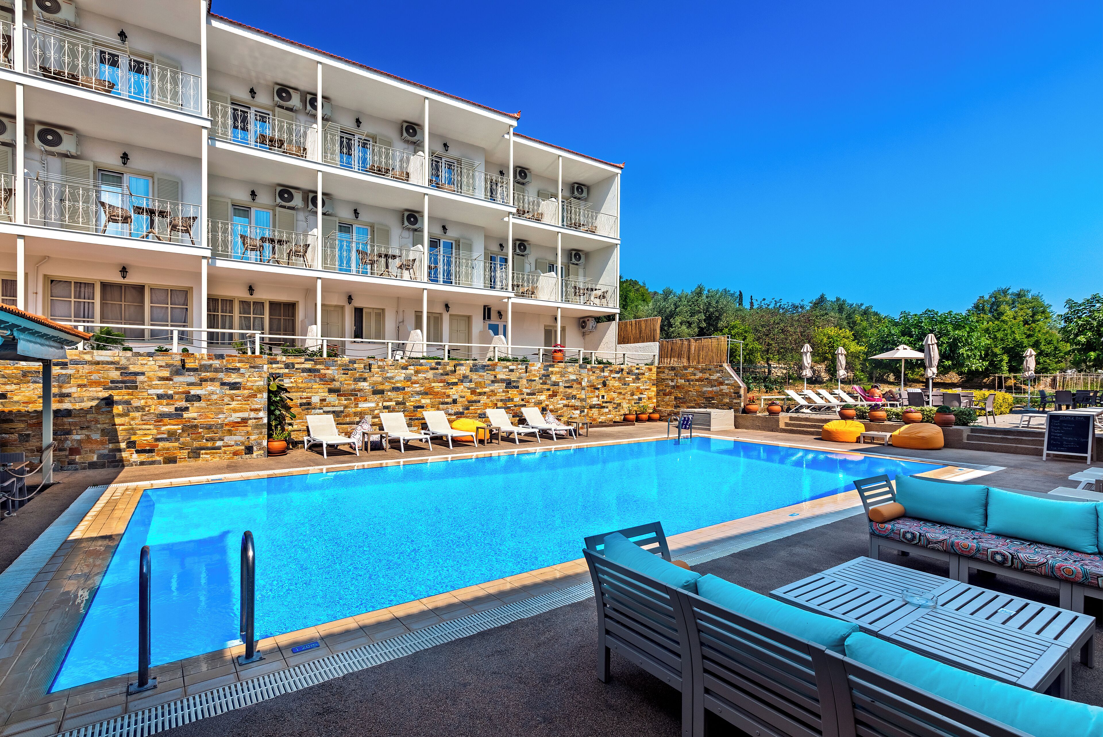 A multi-story hotel with a swimming pool, outdoor seating, and a stone wall.