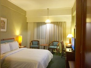 A hotel room with a large bed, two chairs, a small table, a television, and a window with curtains. - Paragon Gallery Hotel Jakarta (Jakarta)