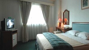 A hotel room with a bed, a television, a desk with a lamp, and a window with curtains. - Paragon Gallery Hotel Jakarta (Jakarta)