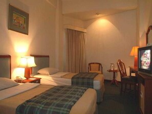 Een hotelkamer met twee bedden, een televisie, een stoel en een lamp.