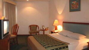 A hotel room with a bed, a chair, a television, and a lamp. - Paragon Gallery Hotel Jakarta (Jakarta)