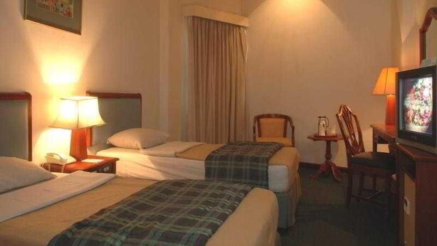 A hotel room with two beds, a television, a chair, and a lamp. - Paragon Gallery Hotel Jakarta (Jakarta)