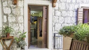 Un edificio de piedra con una puerta de madera que da al interior. Hay plantas en macetas afuera y un banco dentro.