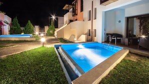A modern outdoor swimming pool area with a well-lit deck and a staircase leading to a second-floor balcony.