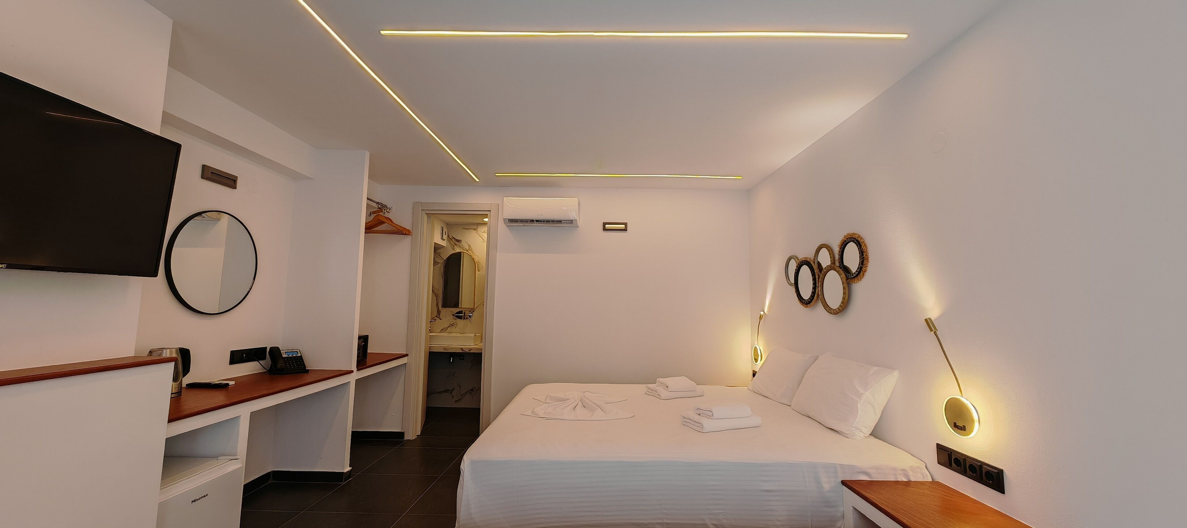 Una habitación de hotel moderna con cama, mesita de noche, televisor montado en la pared y un espejo.
