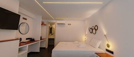 Una habitación de hotel moderna con cama, mesita de noche, televisor montado en la pared y un espejo.