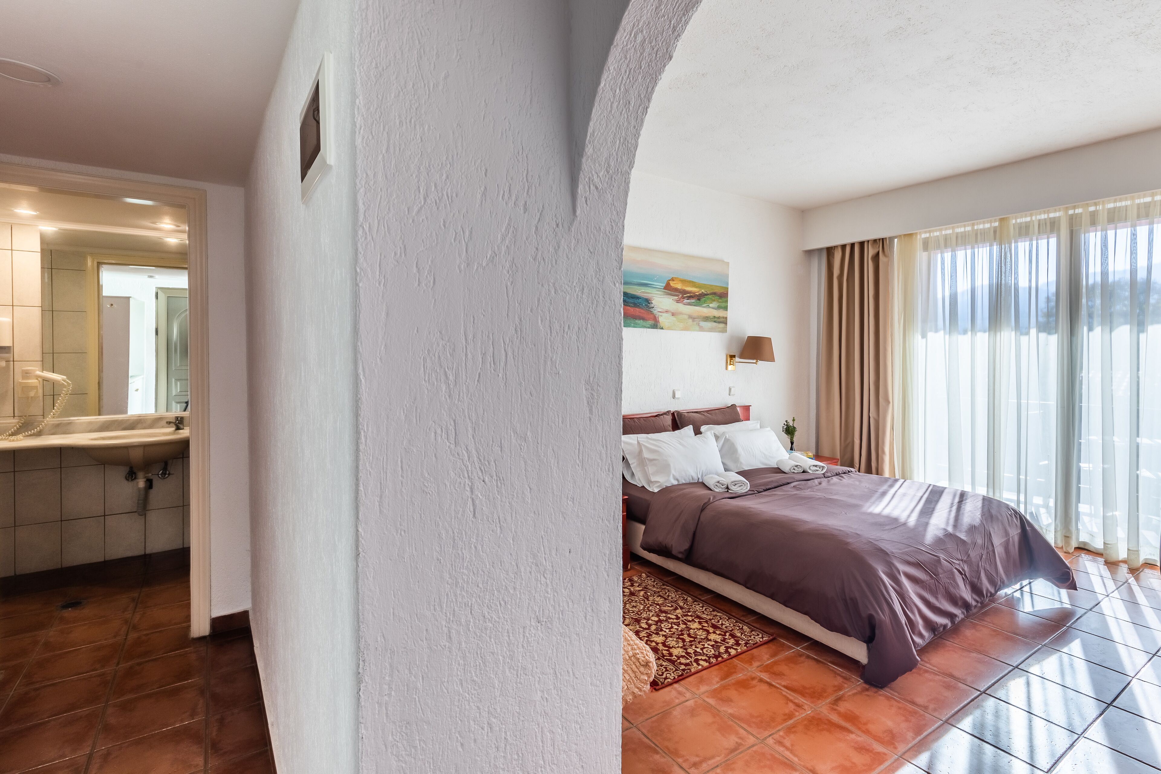 A hotel room with a bed, a bathroom, and a large window.