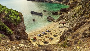 A coastal beach with clear water, rocky cliffs, and beach umbrellas. - Rigas Hotel Skopelos by GHH (Skopelos)
