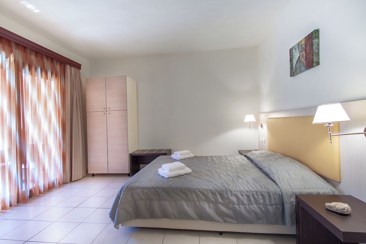A hotel room with a bed, a wardrobe, a nightstand, a lamp, and a painting on the wall.