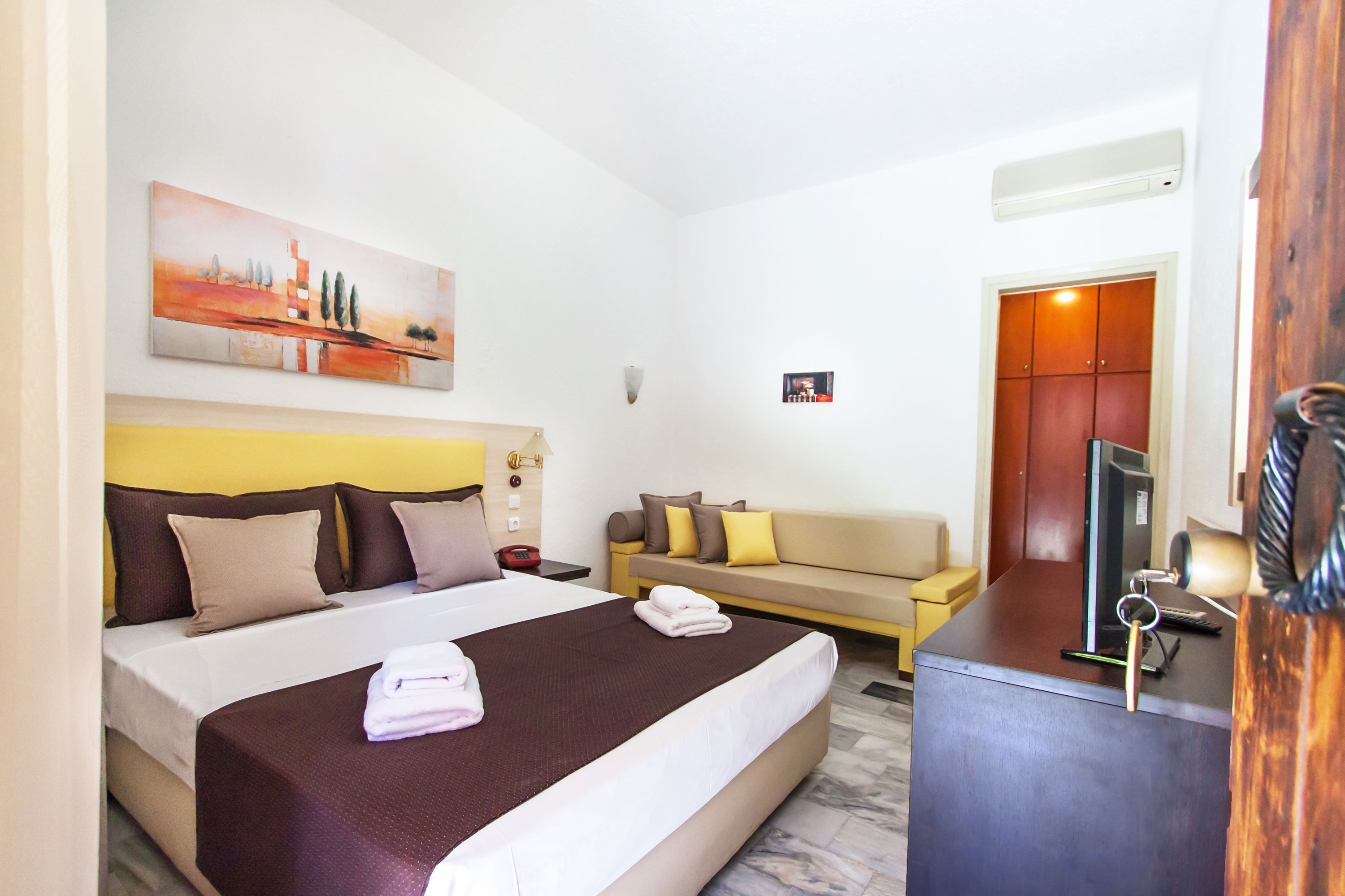 A hotel room with a bed, a sofa, a desk, and a painting on the wall.