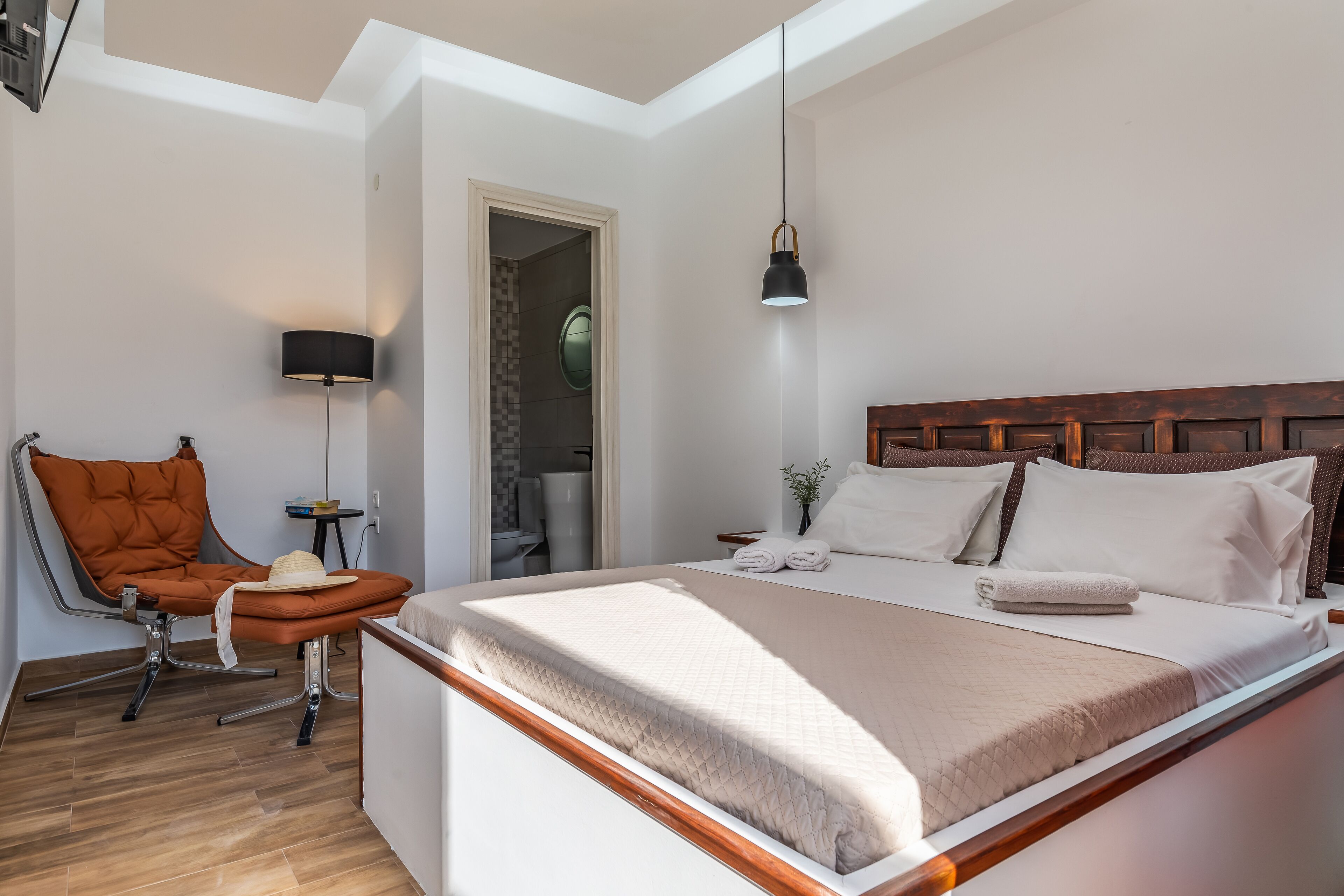 Une chambre moderne avec un grand lit, une chaise, une table de chevet et une lampe.