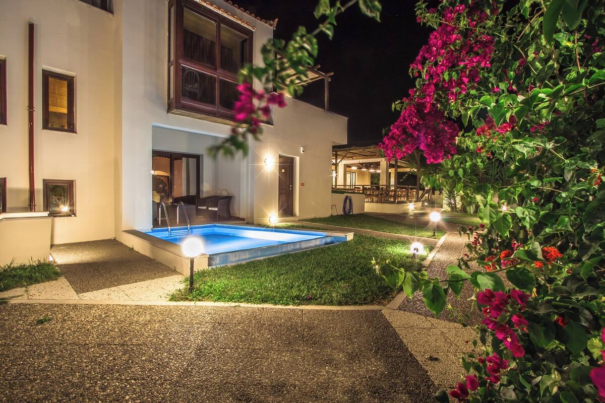 A modern two-story house with a swimming pool, outdoor seating, and a well-lit patio area.